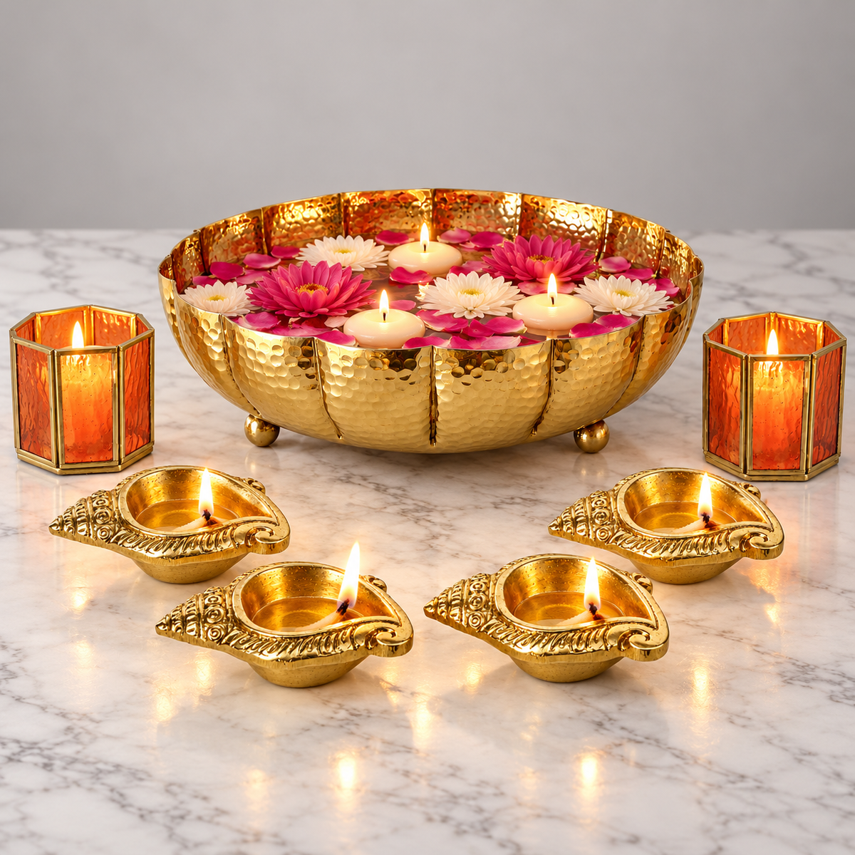 Juhi Urli Festive Centrepiece Set on marble - gold urli with floating flowers and tealights, four brass shankh diyas and two orange glass votives