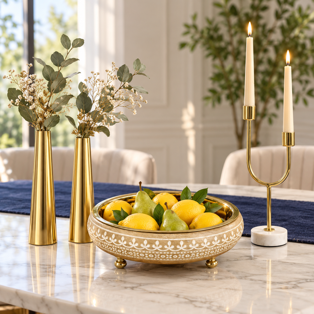 Virasat urli holding pears beside gold slim cone vases and a dual arc candle holder on a dining table