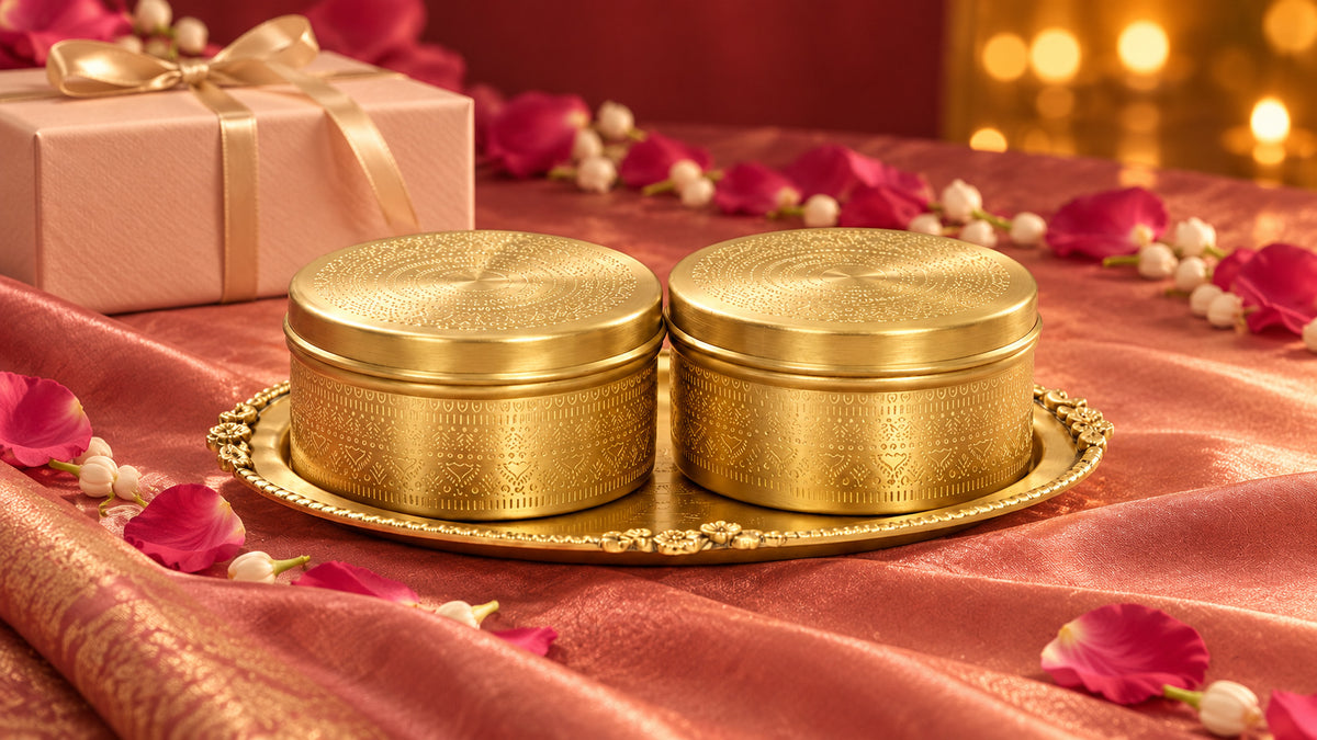 Pair of etched brass sweet boxes on an ornate brass tray beside a gift box and rose petals