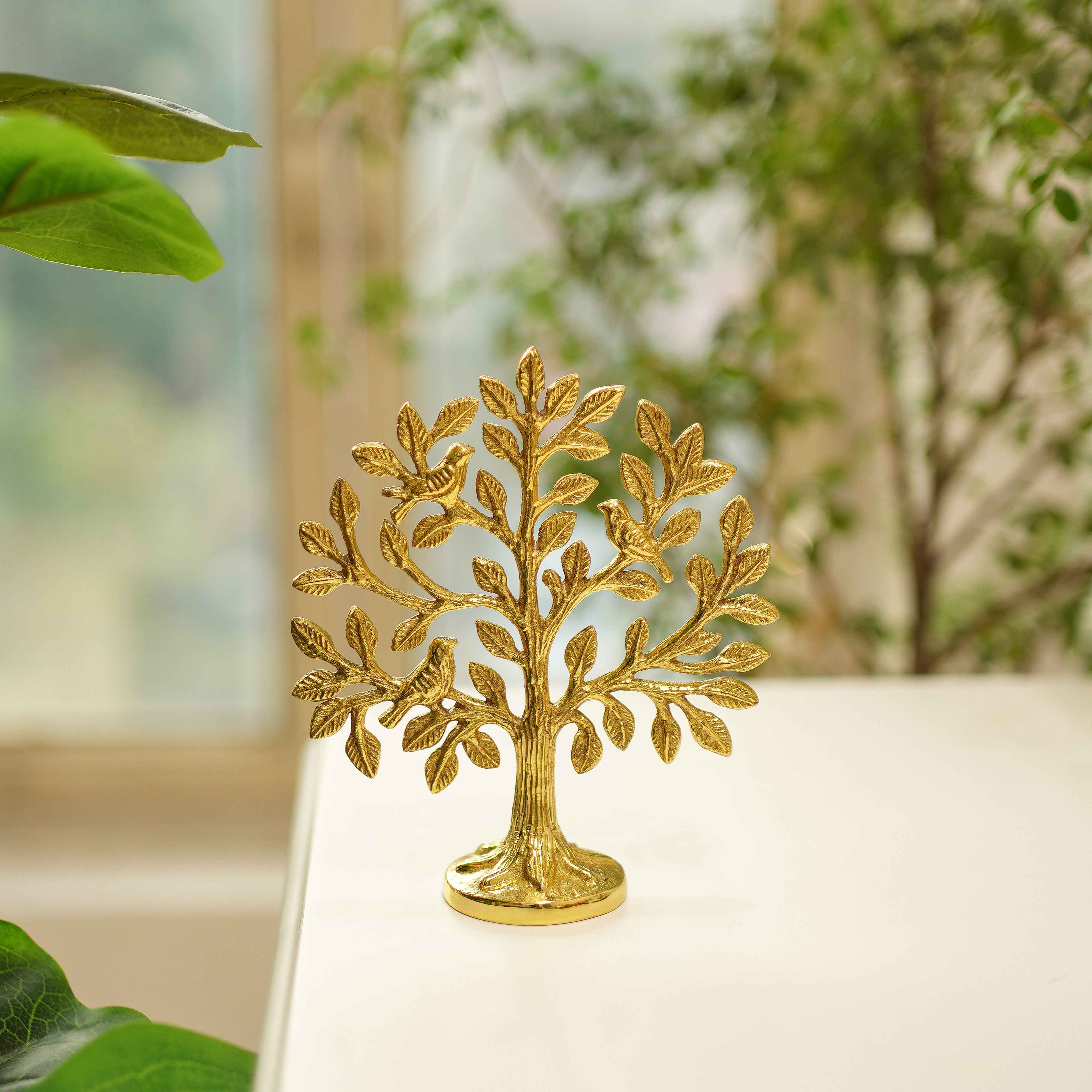 brass tree-shaped decorative item on a white surface with green leaves in the background
