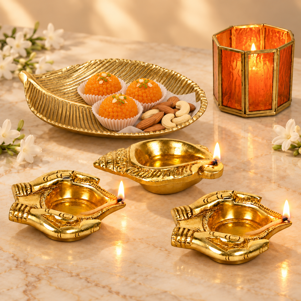 Diwali Ghar Ki Shobha gift set - gold leaf platter with laddoos and nuts, an orange glass votive, two brass bhakti deepak lamps and a shankh diya lit on marble