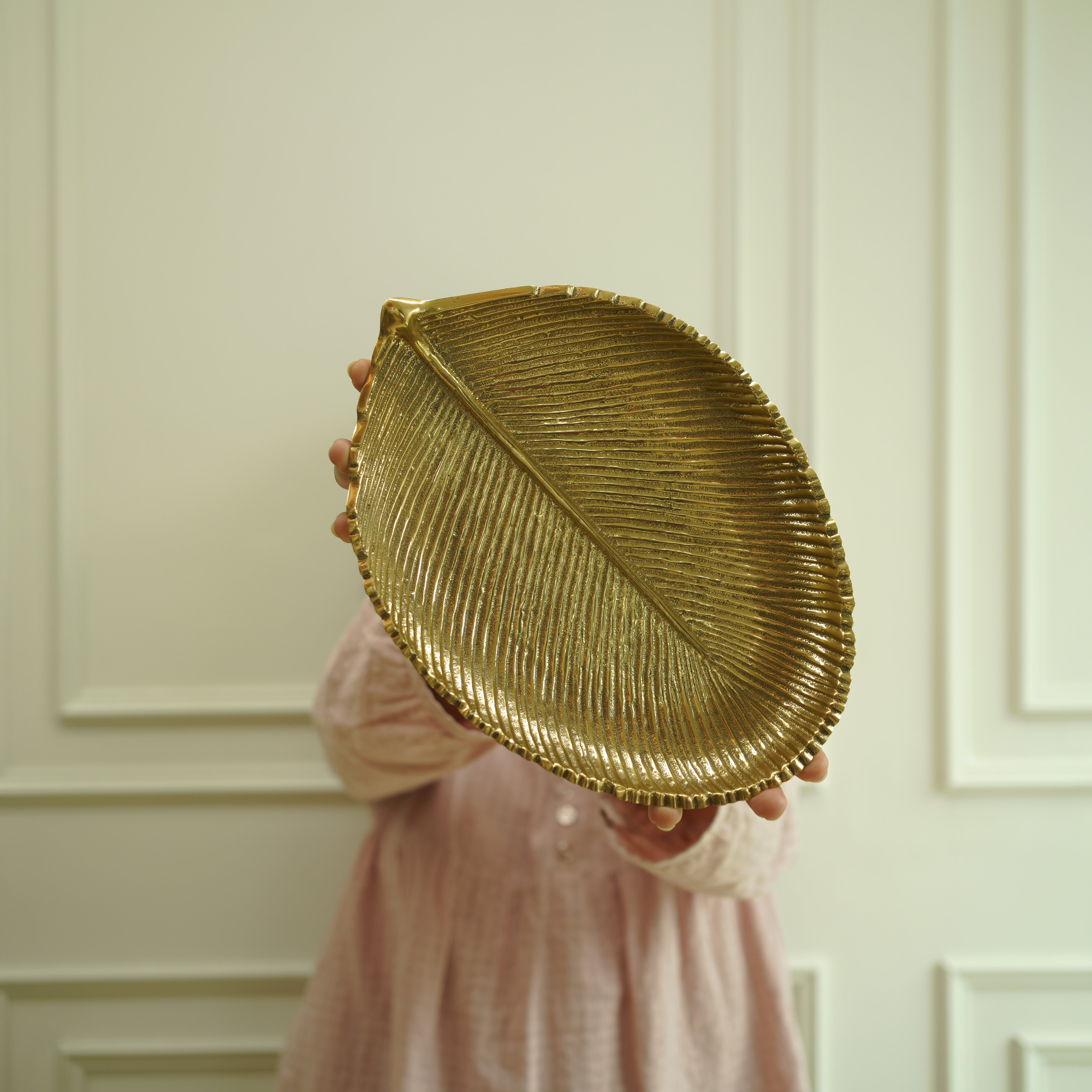 Gold leaf-shaped decorative plate held by a person against a neutral wall.