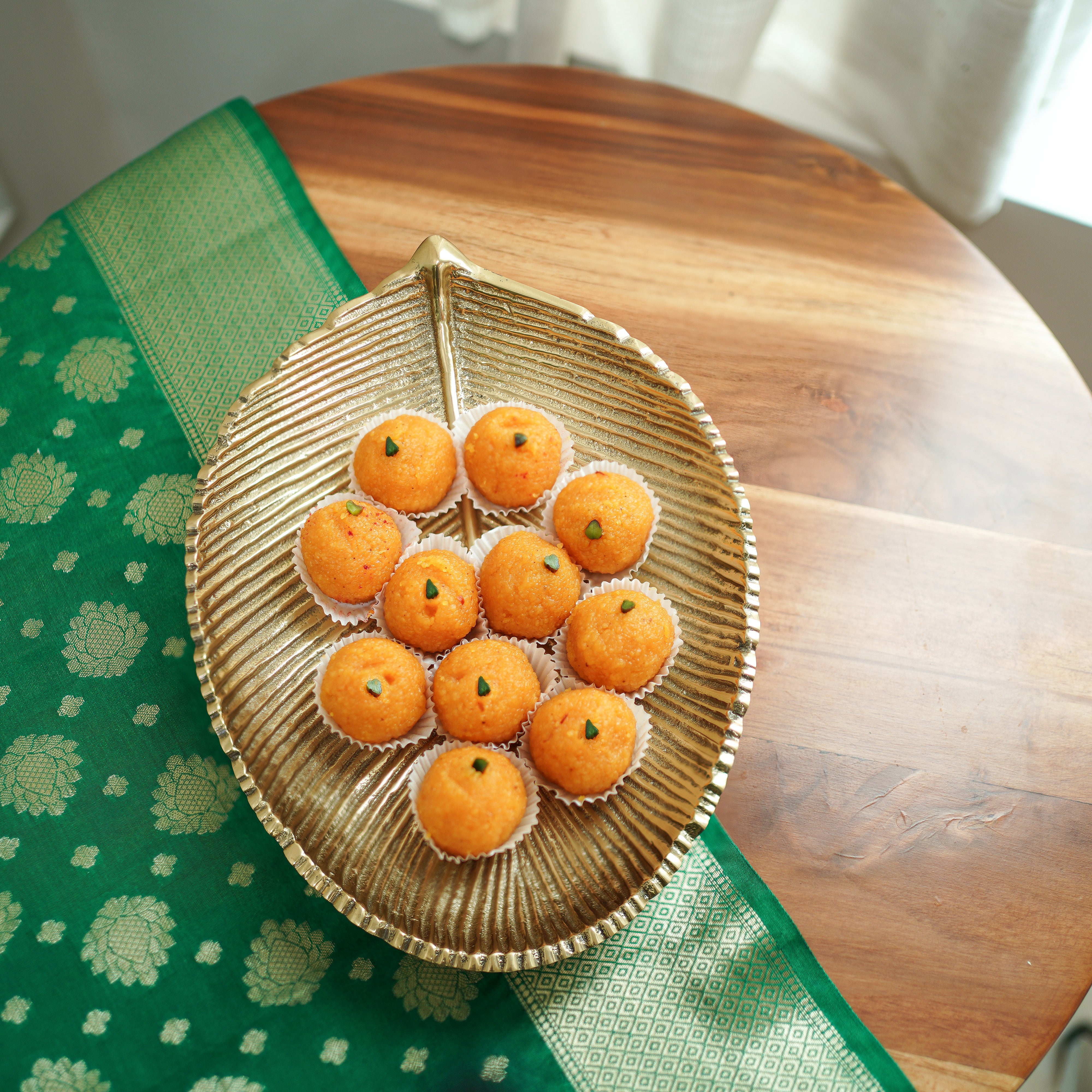 Decorative leaf-shaped plate with Ladoo on a wooden table with green fabric.