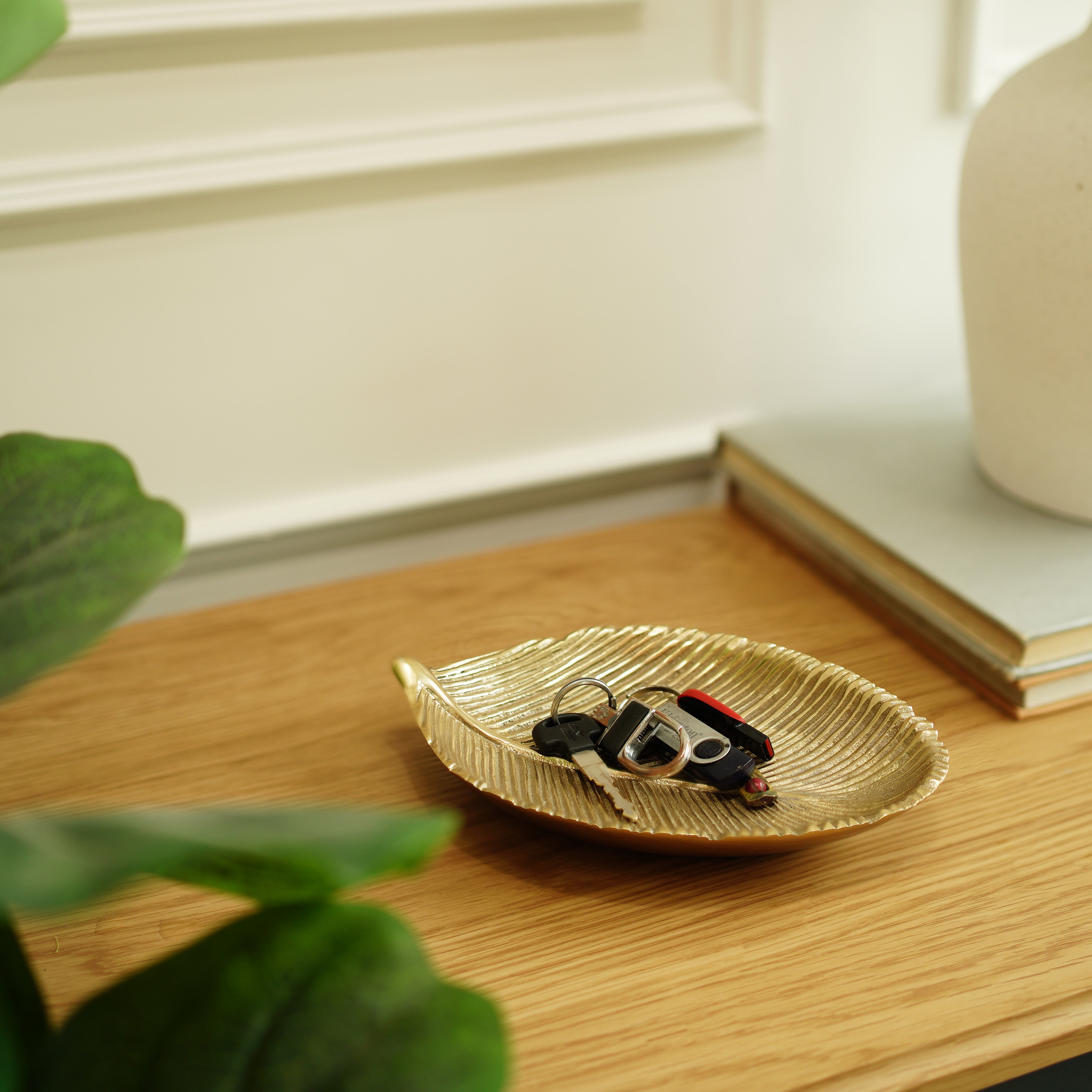 Gold leaf-shaped tray with keys on a wooden surface, with a blurred background
