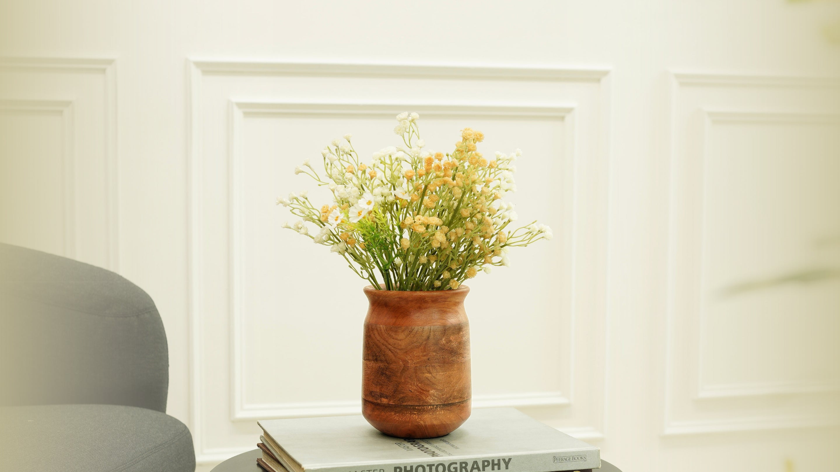 Vase with yellow flowers on a stack of books against a white wall