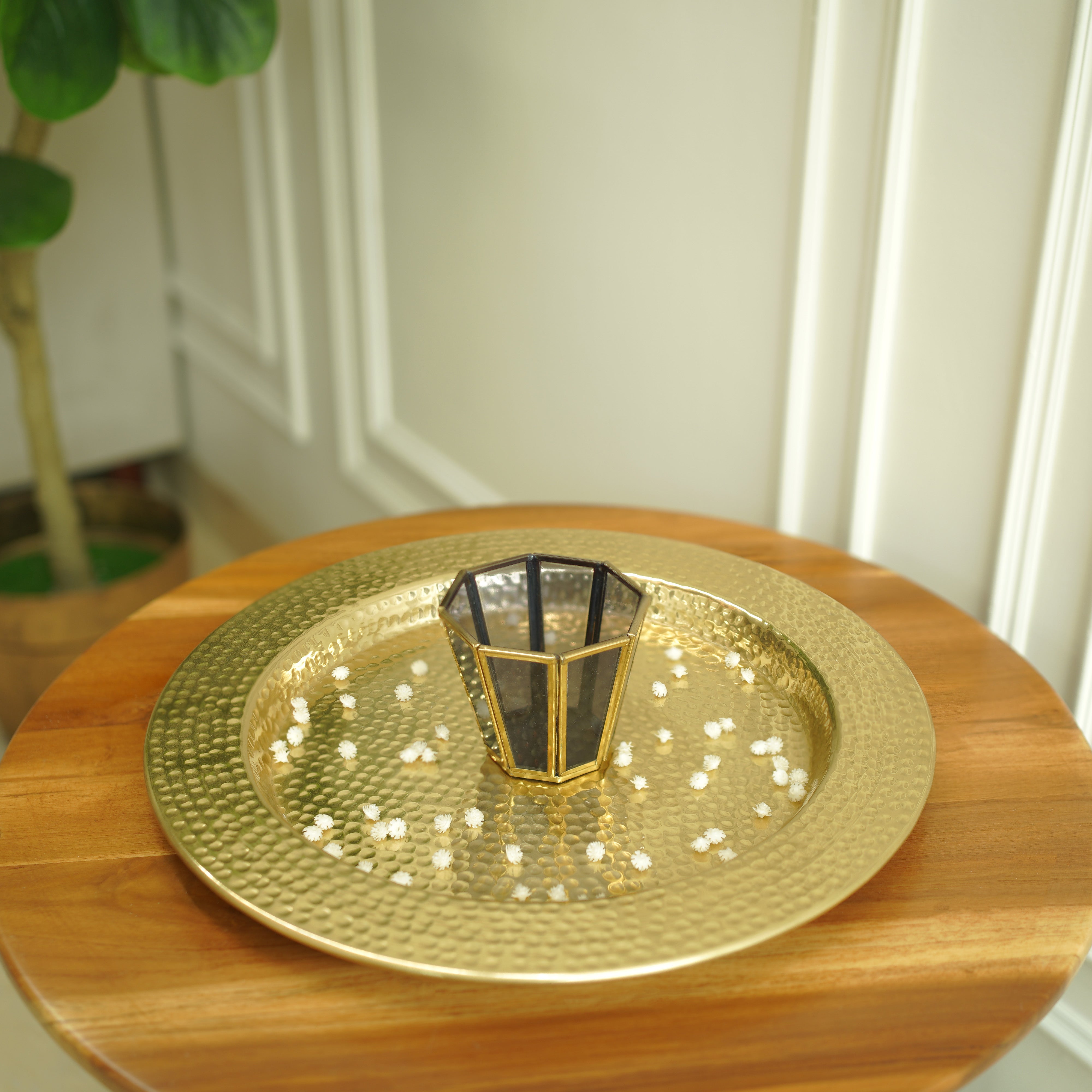 Gold decorative plate with a central candle holder on a wooden surface.
