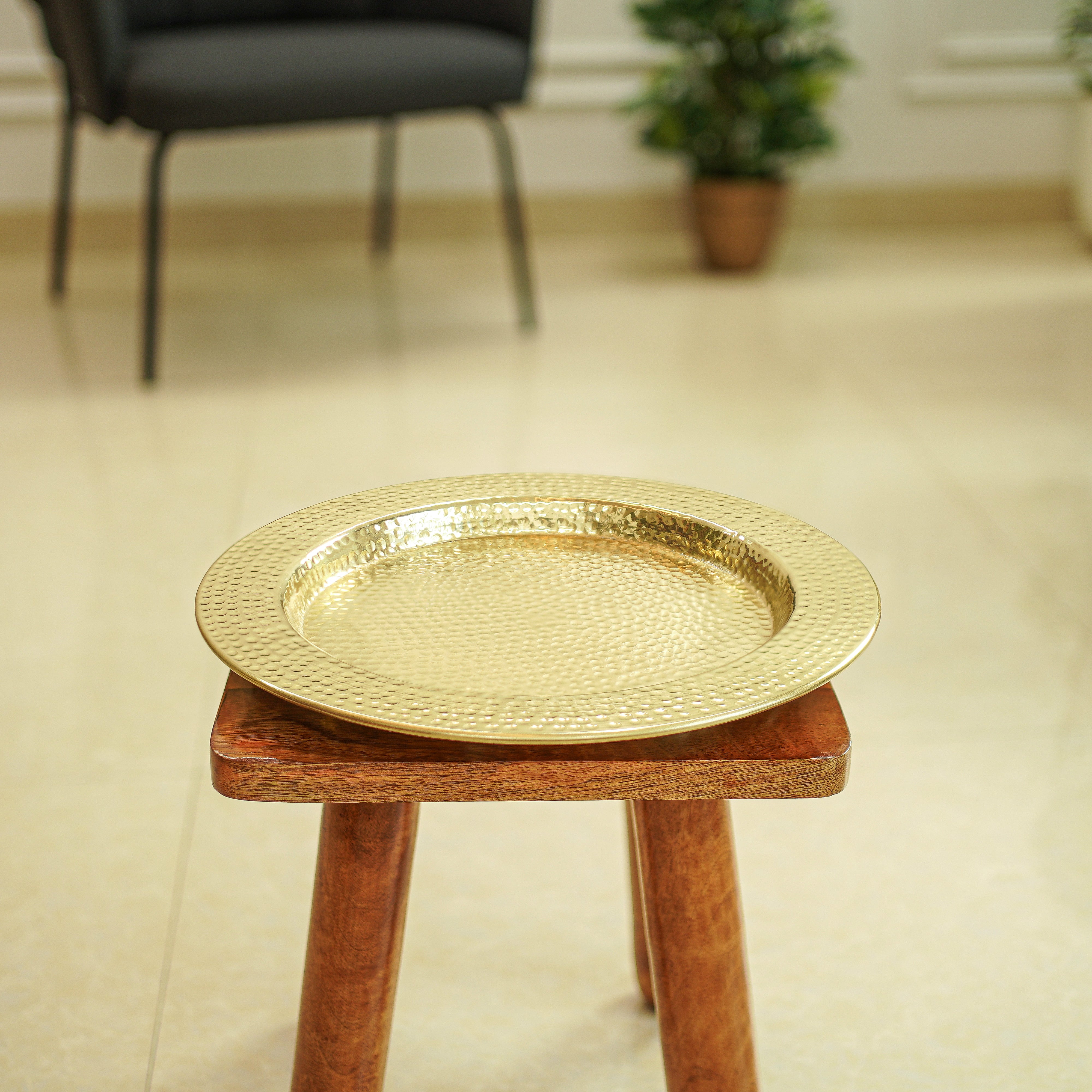 Gold decorative tray on a wooden stool in a room with a blurred background