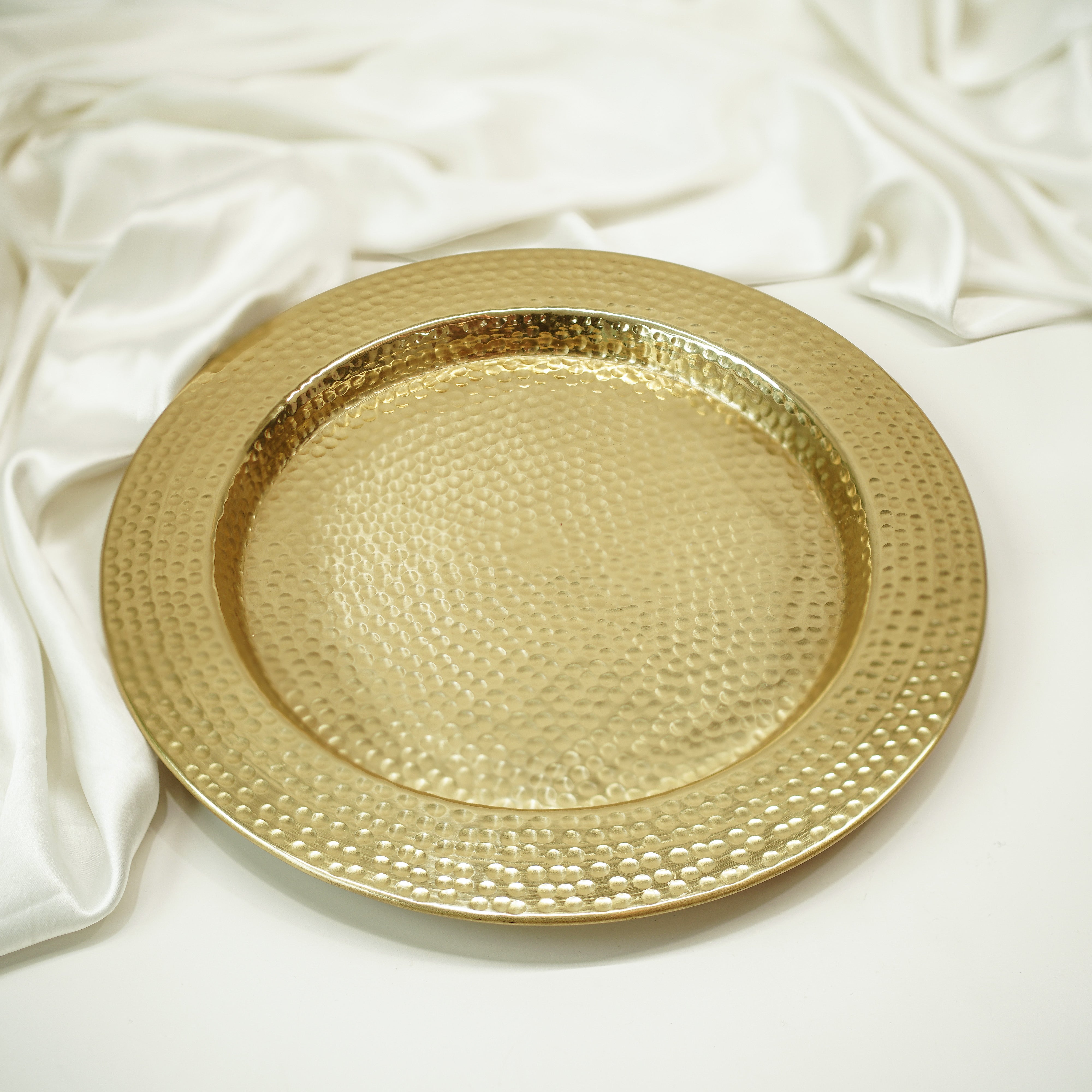Gold decorative plate with textured surface on a white fabric background