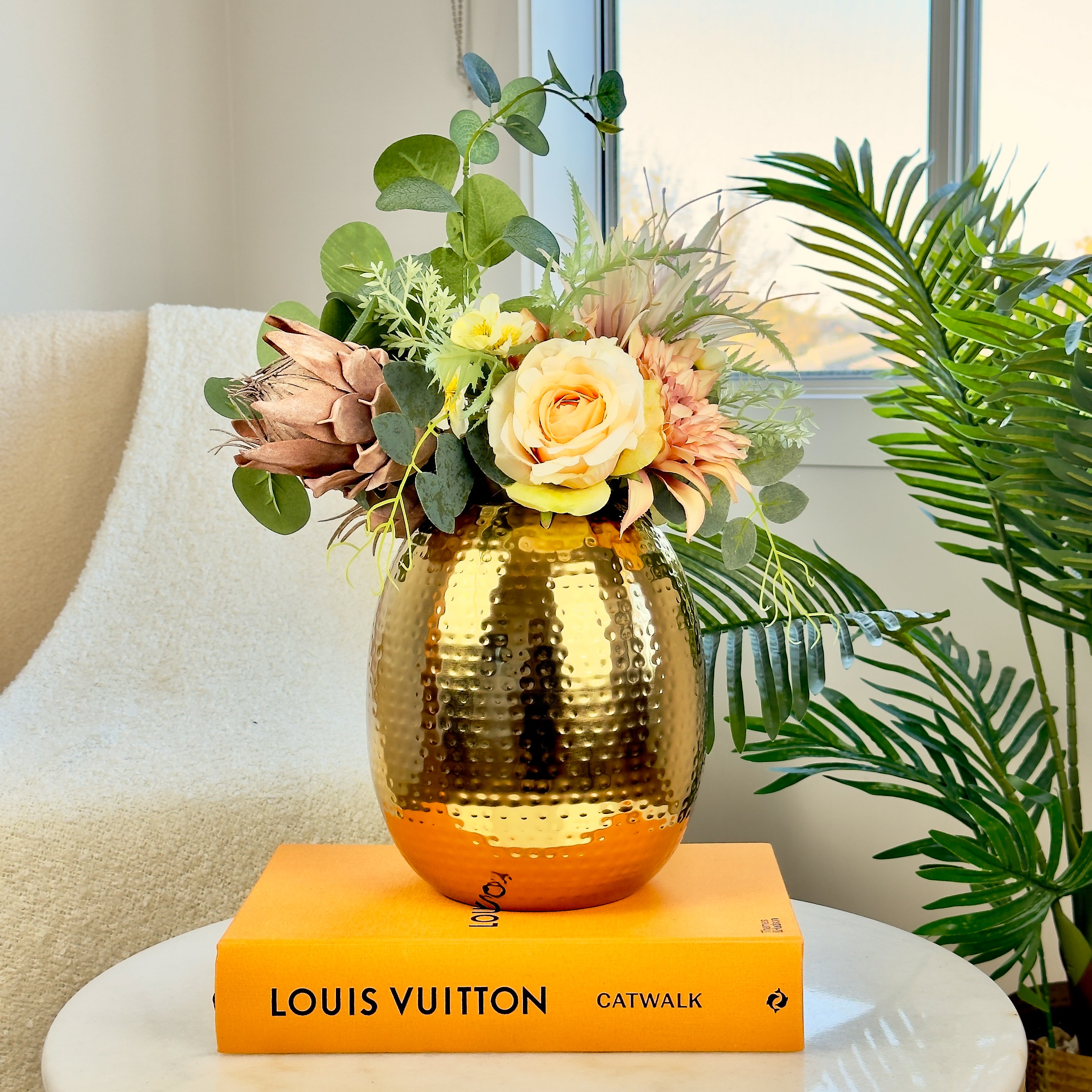 Product image of the Oval Vase Hammered Gold from Indian Impressions, featuring a sleek oval design with a textured hammered finish. Crafted with a polished gold-tone, this vase is perfect for displaying flowers or as a standalone décor piece. Ideal for Vastu, home décor, or gifting, adding elegance and sophistication to any space.
