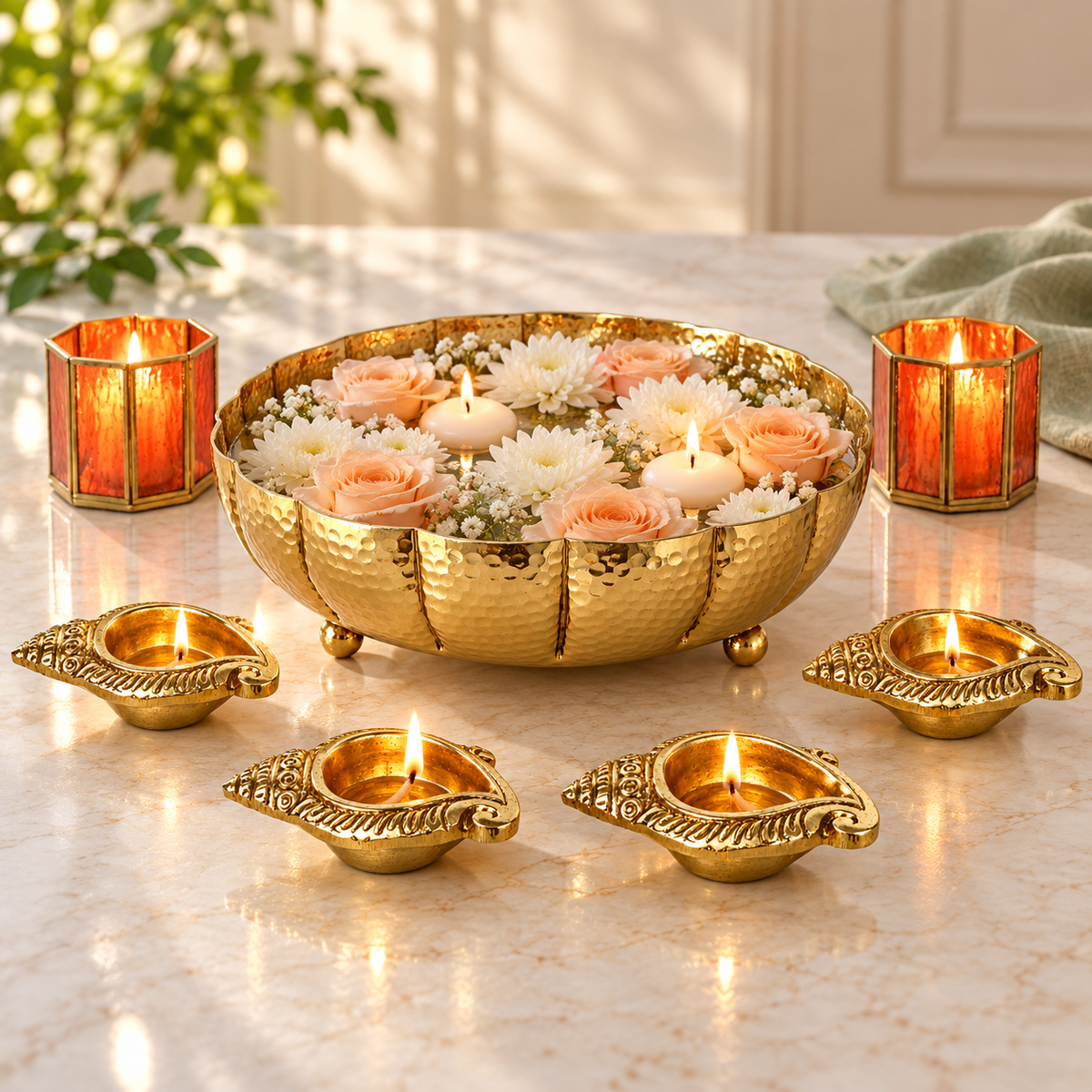 Juhi gold urli with pale roses and floating tealights beside brass shankh diyas and orange votives on a kitchen bench