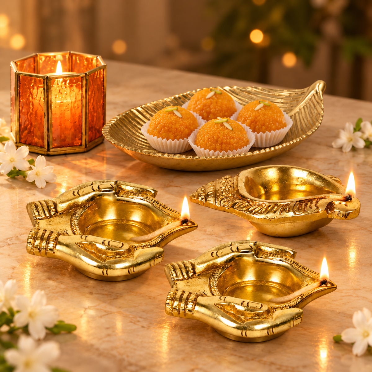 Gold leaf platter filled with dry fruit beside a lit orange glass votive and three brass oil lamps