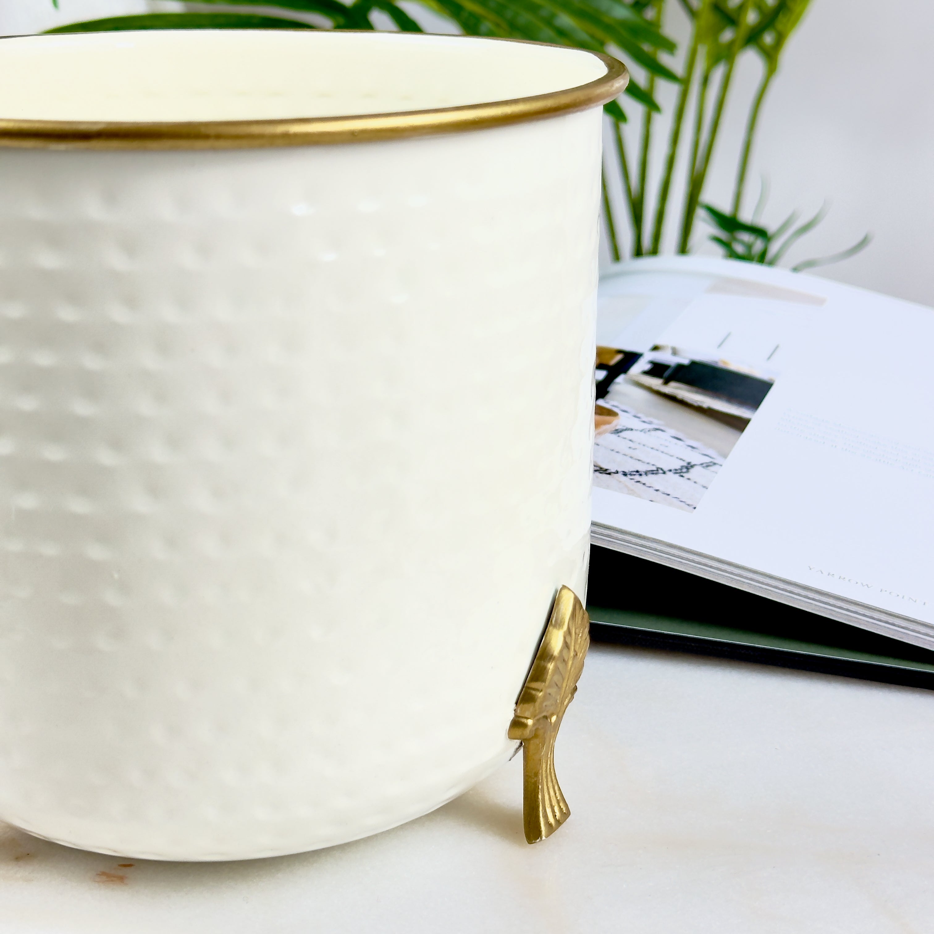 Product image of a Metal Hammered Gold Rim Leaf Leg Planter in White from Indian Impressions, featuring a sleek white body with a hammered texture and a gold rim for an elegant finish. Supported by sturdy leaf-patterned legs, this planter is ideal for enhancing Vastu energy, modern home décor, or gifting, adding sophistication to any space.