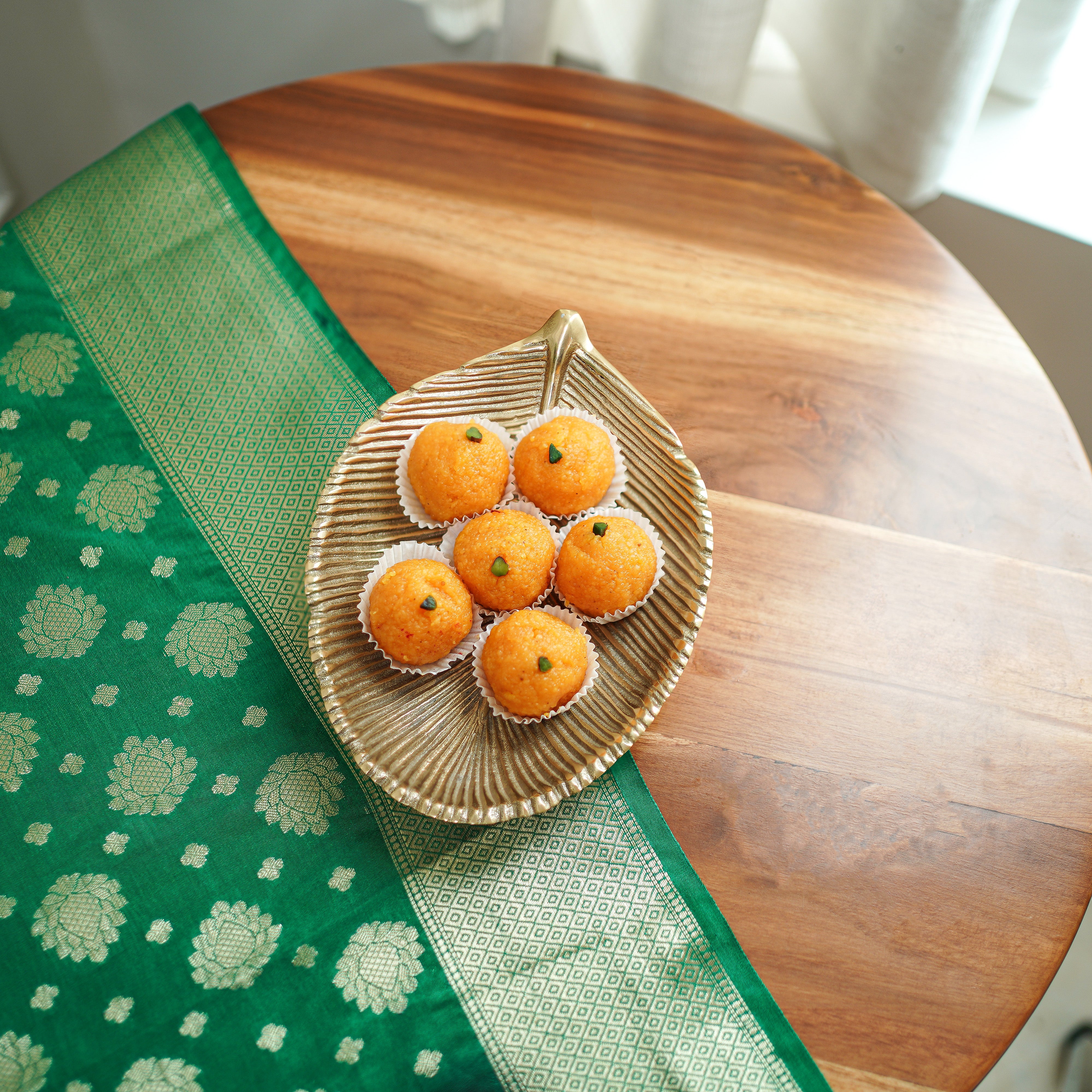 Woven leaf-shaped plate with Ladoo on a wooden table with a green fabric.