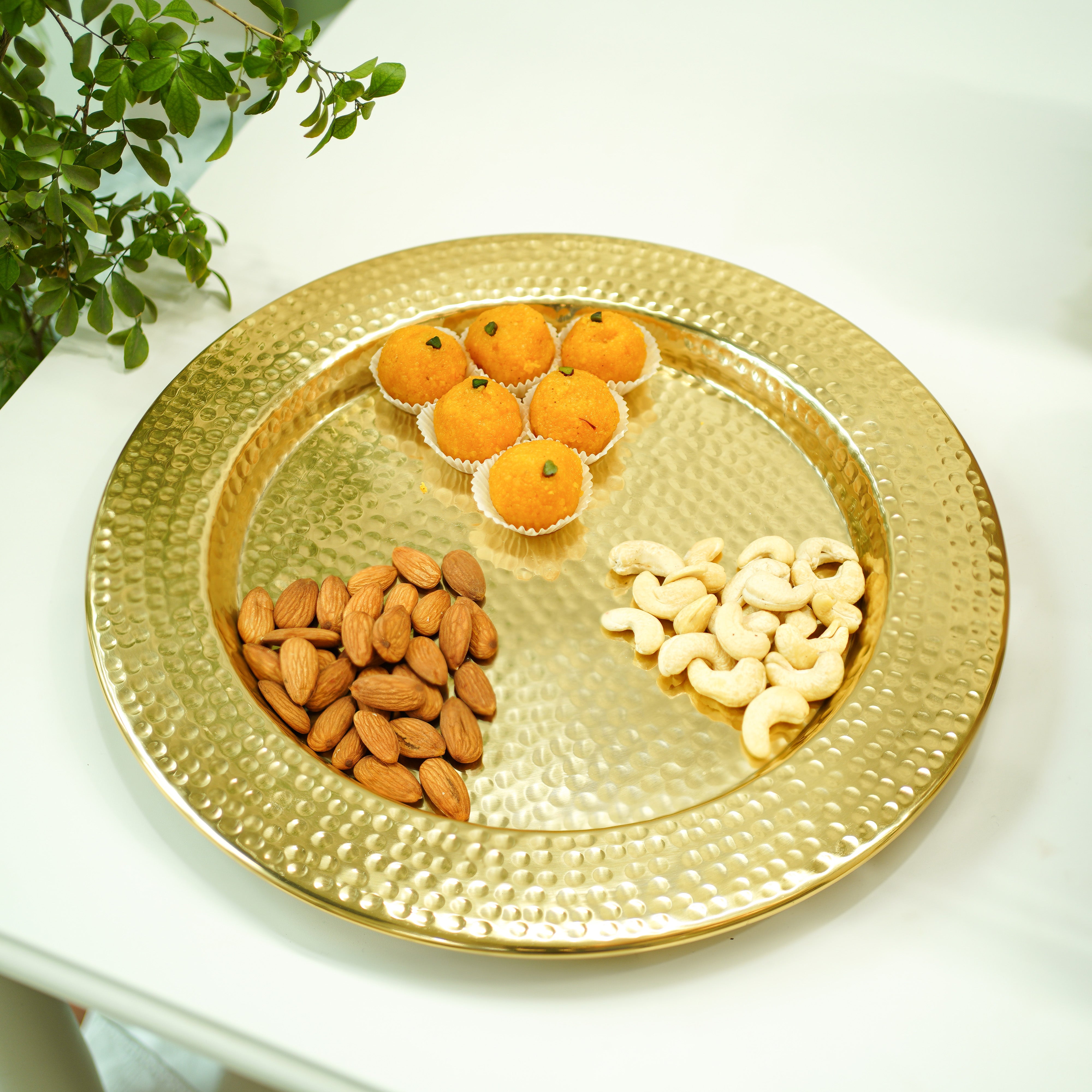 Gold tray with almonds, cashews, and oranges on a white surface.