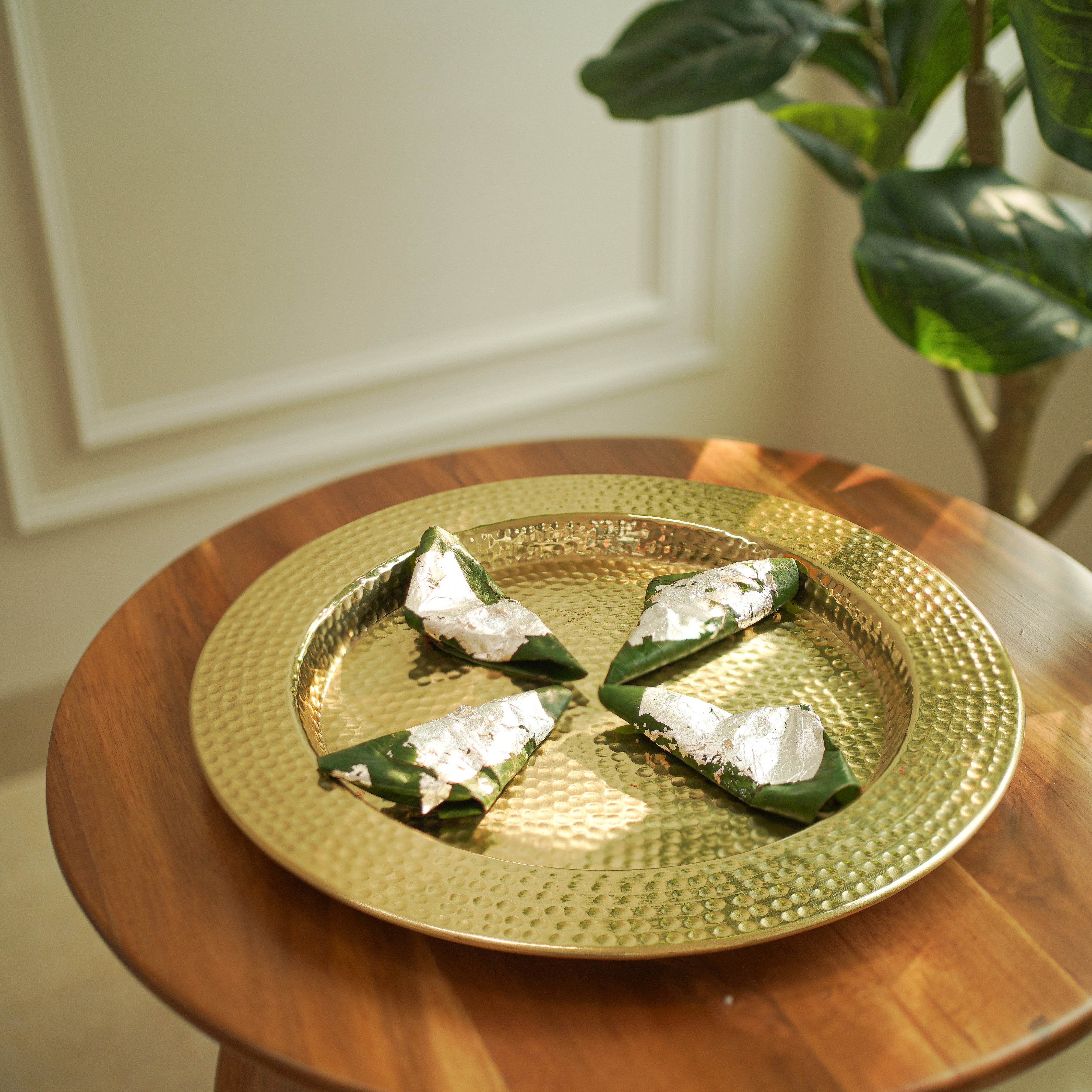 Gold plate with food items on a wooden table, plant in the background