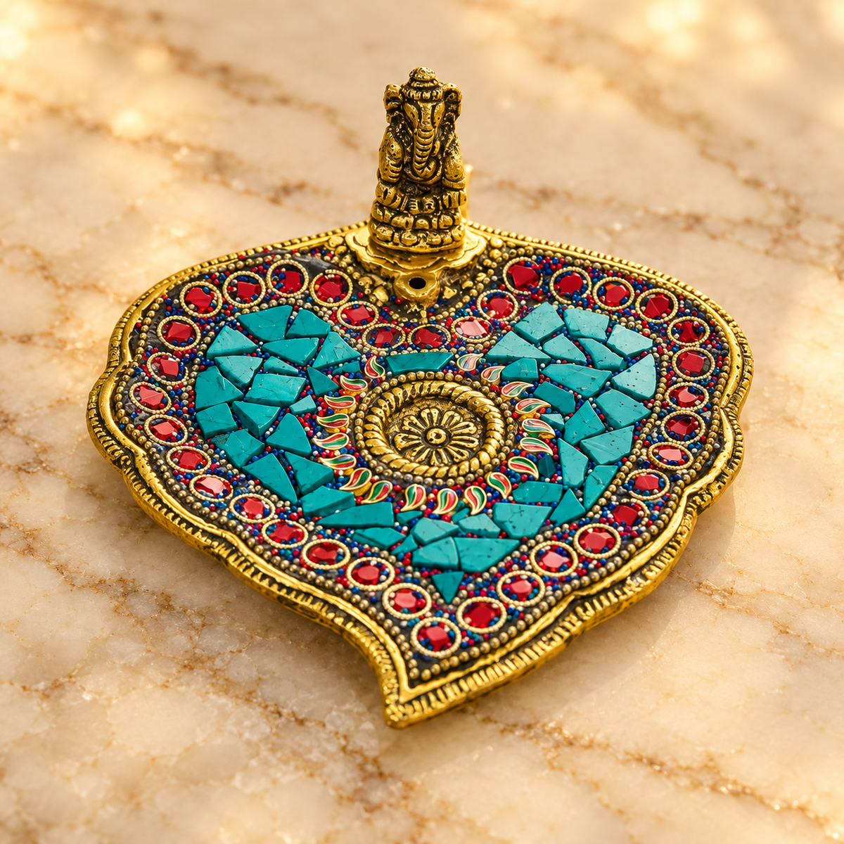 Close-up of Ganesha figurine, turquoise inlay and red studs on metal incense stand